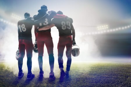 The back view of three caucasian fitness men as american football players on stadium background